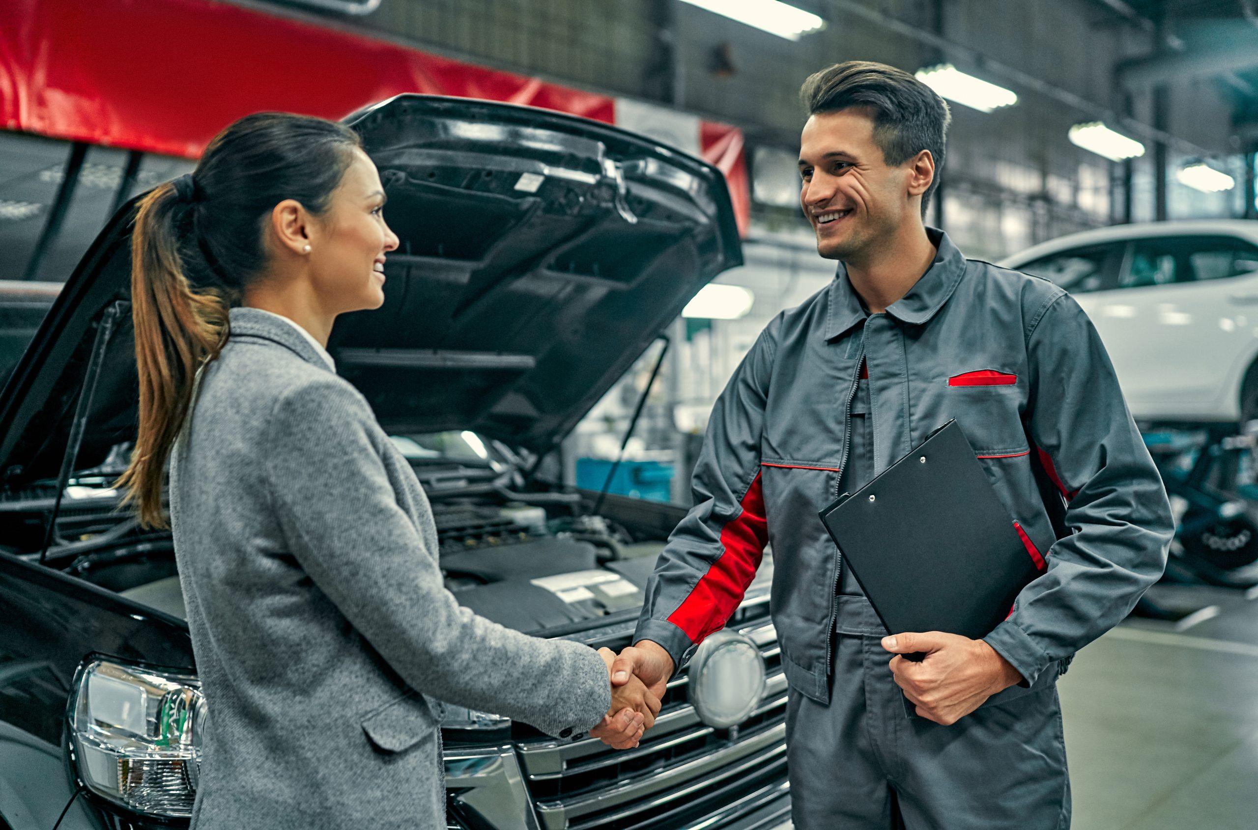 Beautiful businesswoman and auto service mechanic shaking hands. Car repair and maintenance. Shop owner shaking hands with a buyer after successfully completing a business sale, symbolizing trust and agreement in the transaction.