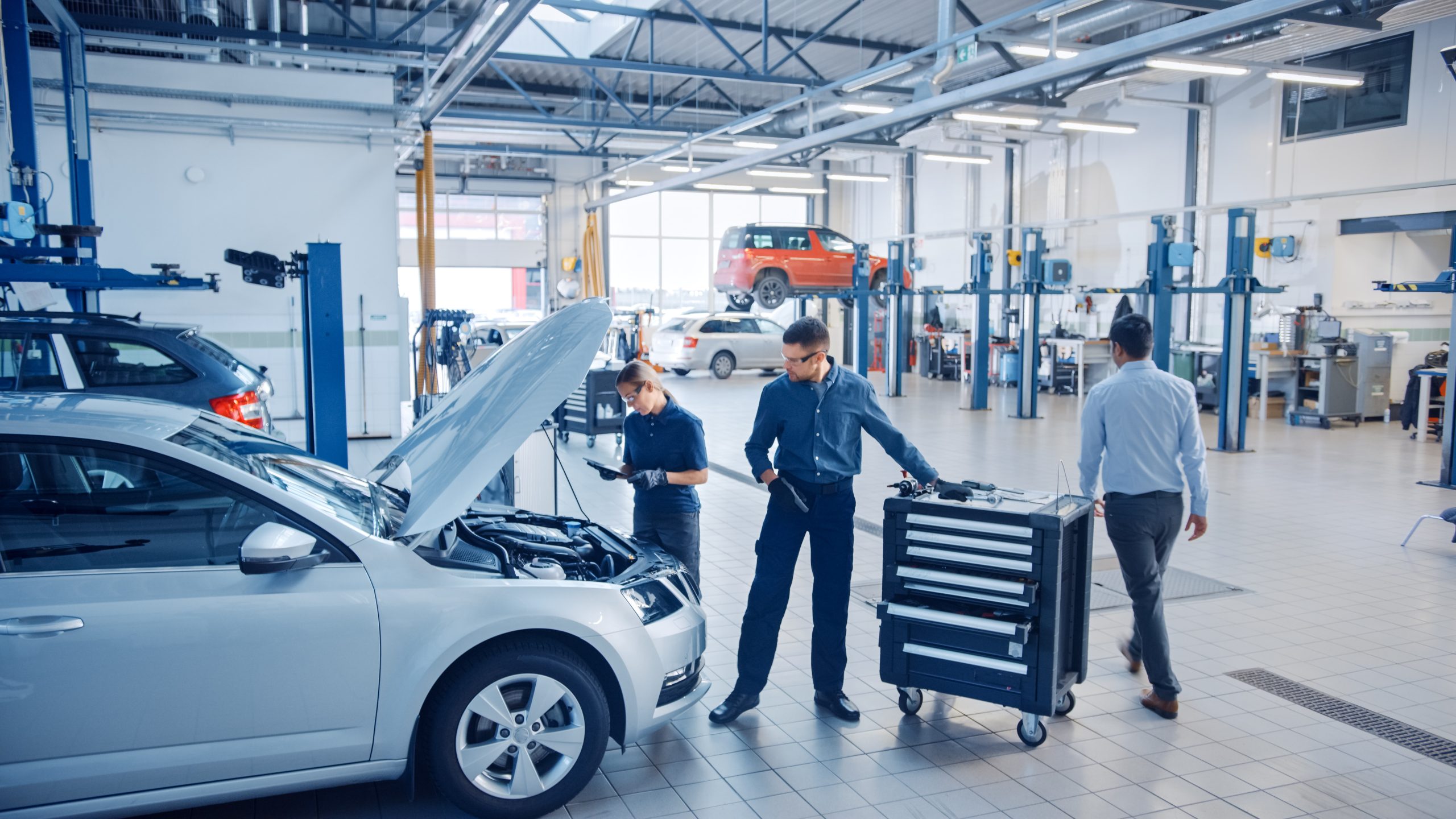 Auto repair technician performing a digital vehicle inspection on a car, using a tablet to check maintenance items in a modern repair shop.