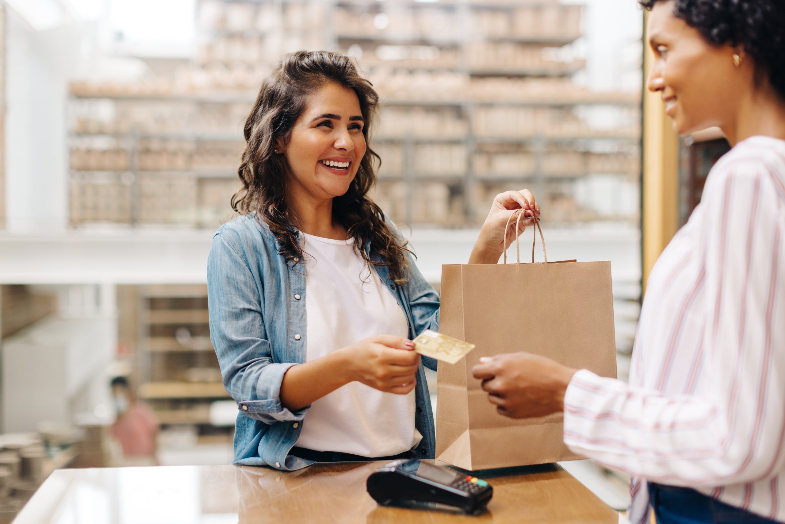 Happy female customer paying with a credit card in a ceramic store Happy shopper at checkout, representing the power of customer retention through positive in-store experiences.